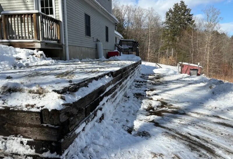 Snow-covered house with wooden retaining wall.