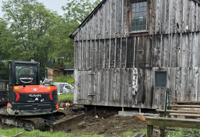 Old barn with a small excavator nearby.